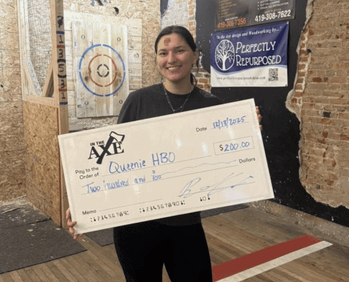 Woman smiling while holding oversized check for HBO donation at Fostoria event.