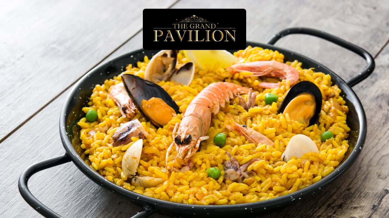 Seafood paella with shrimp, mussels, and clams in a black skillet on wooden surface.