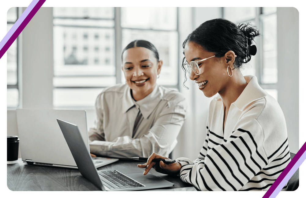 Two women collaborating on laptops at work.