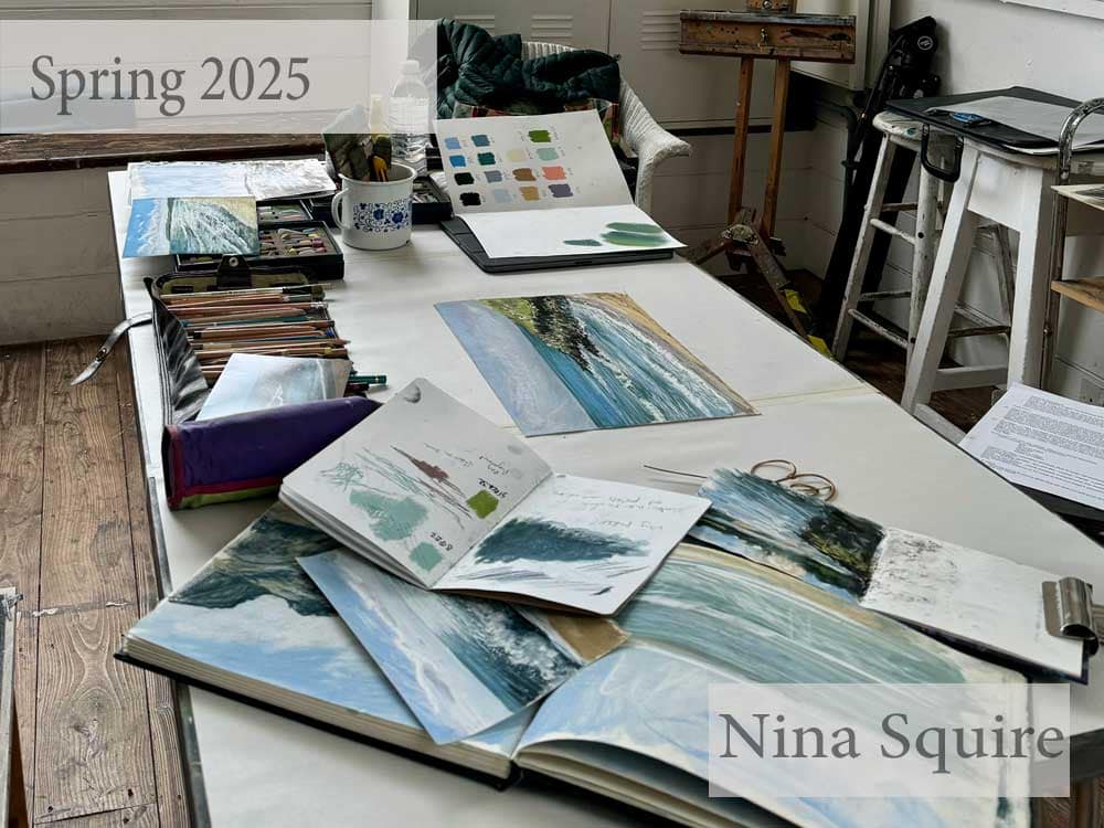 Art workspace with pastel paintings and supplies by Nina Squire.