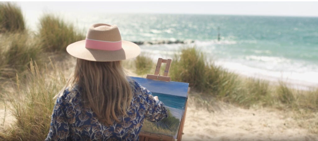 Nina Squire painting outdoors by the seaside with a canvas and easel.
