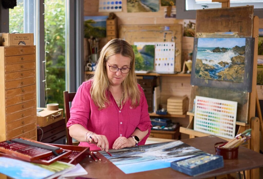 Nina Squire working on a landscape painting in her art studio.