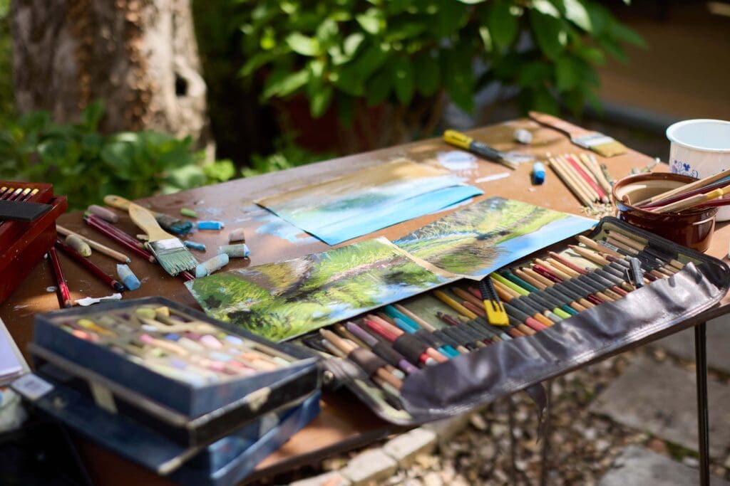 Art supplies and landscape paintings on outdoor table by Nina Squire.