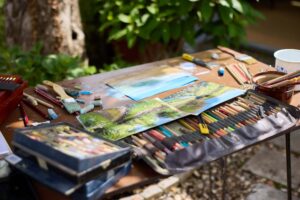 Art supplies and landscape paintings on outdoor table by Nina Squire.