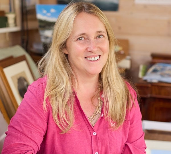 Nina Squire smiling in her art studio with pastel artworks in the background.