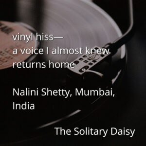 A close-up of a vinyl record playing on a turntable, overlaid with a haiku-style poem and the poet's name, location, and "The Solitary Daisy" publication title.