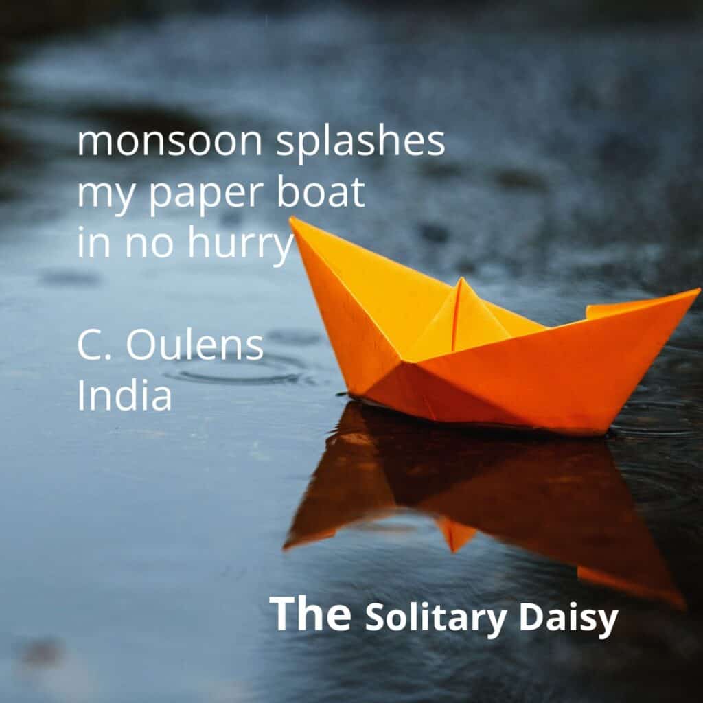 An orange paper boat floats on a rain-soaked surface. Text on the image shows a haiku about a monsoon and the poet’s name, C. Oulens, along with “India” and “The Solitary Daisy.”.