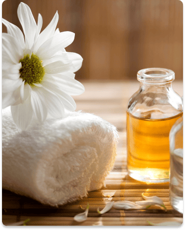 image of massage oil next to a towel with a white flower on top of it.