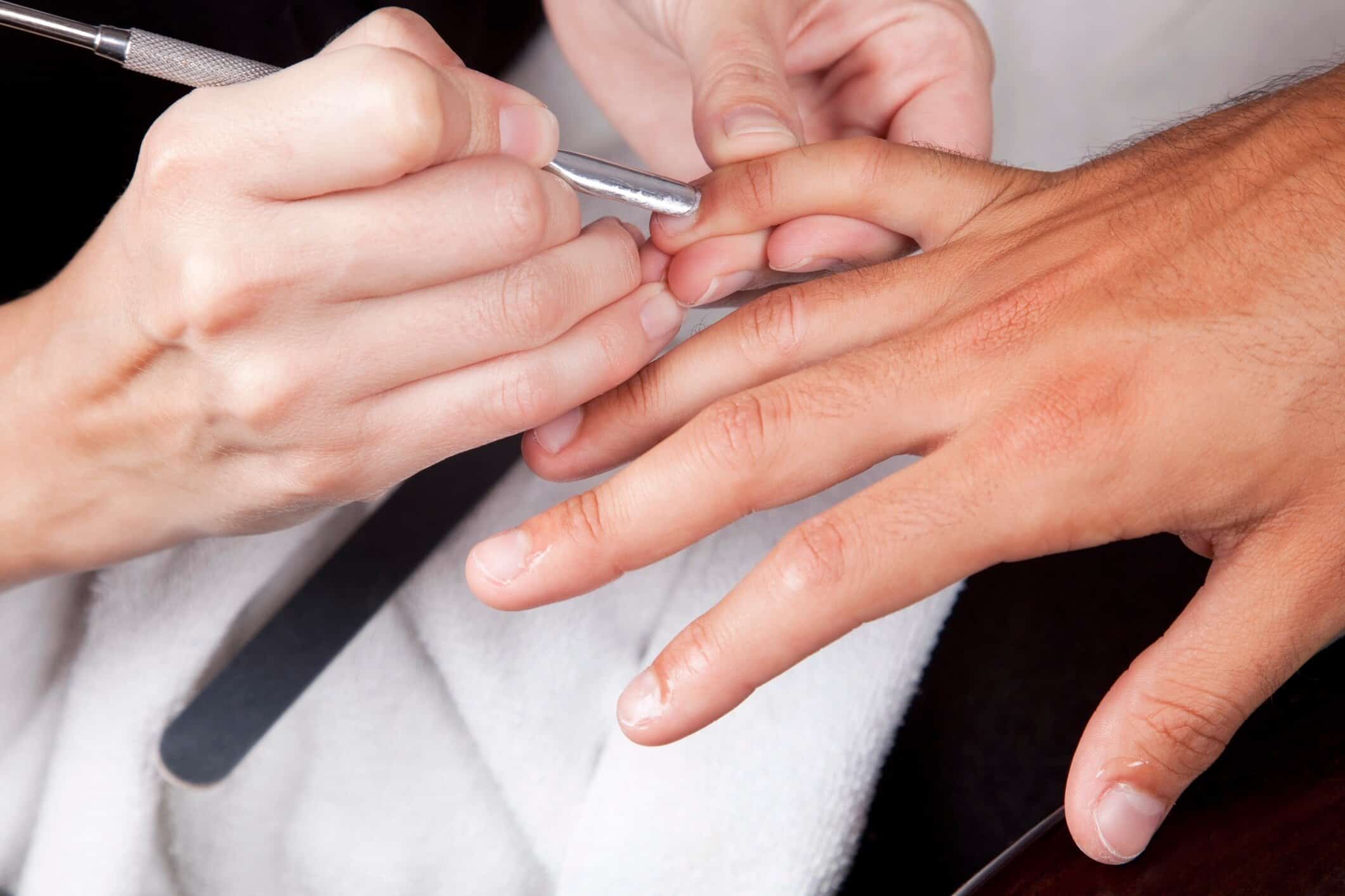 Manicurist applying clear or light pink nail polish to a client's finger over a bowl used for a nail soak.