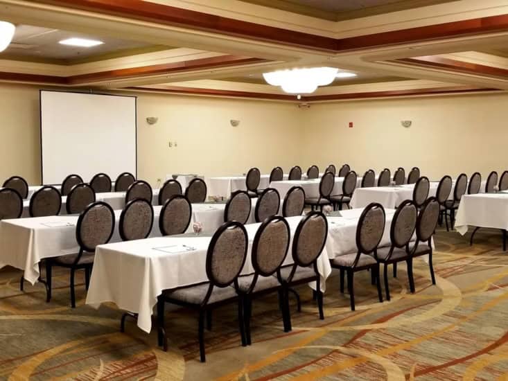 Event room with tables and chairs and a screen for presentations. Gallery Image