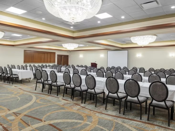 Large meeting room with tables, chairs, and a projector screen. Gallery Image