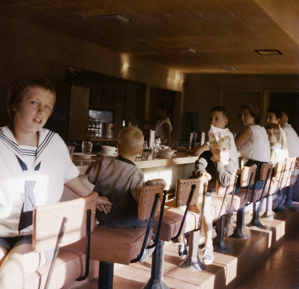 Children seated at a diner counter on bar stools in a vintage 1970s-era restaurant Gallery Image