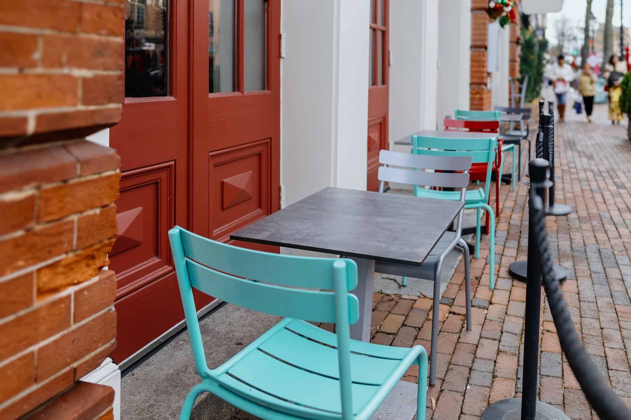 Colorful outdoor café patio with teal and red metal chairs along a brick sidewalk