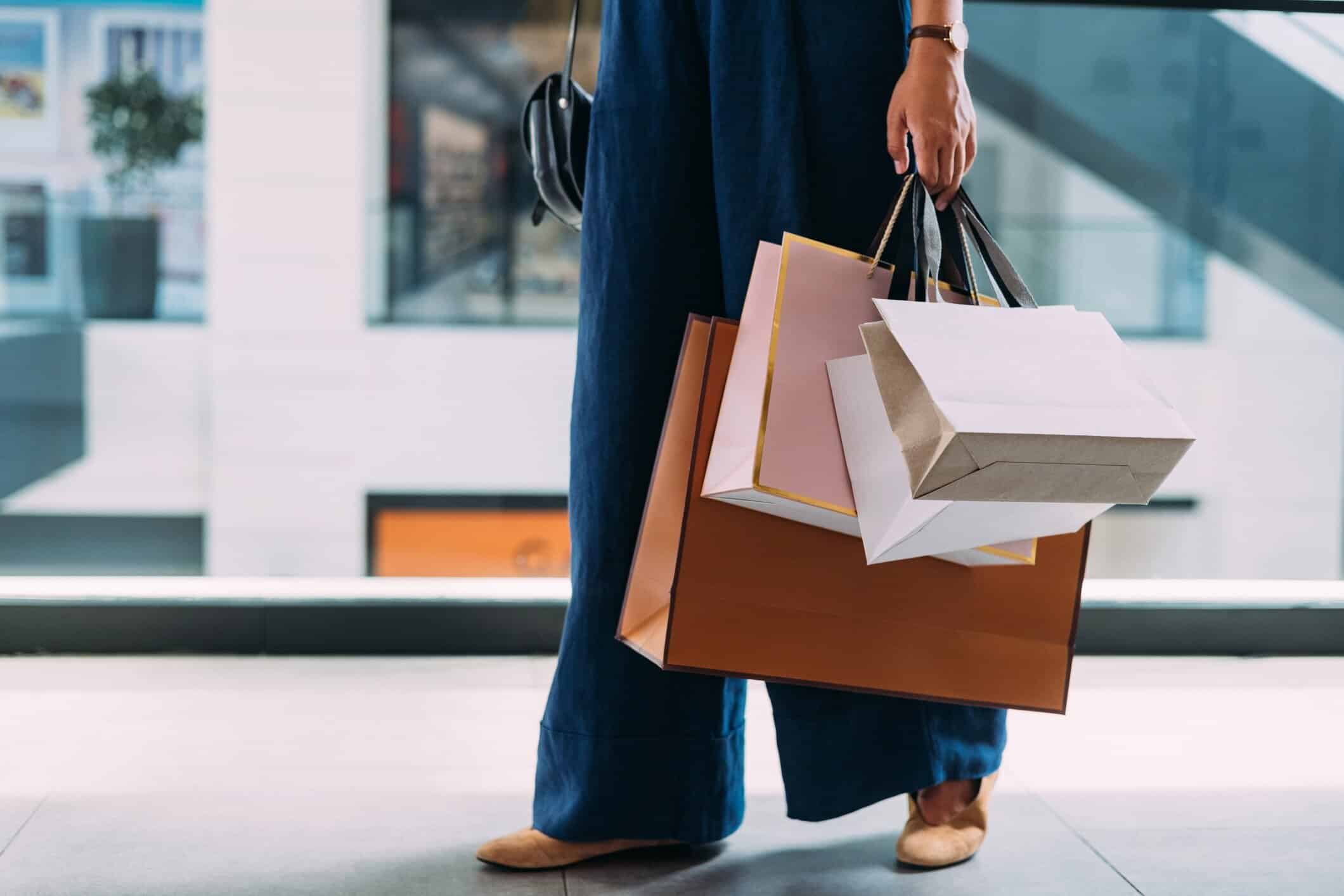 Woman carrying multiple luxury shopping bags while walking through an upscale shopping center
