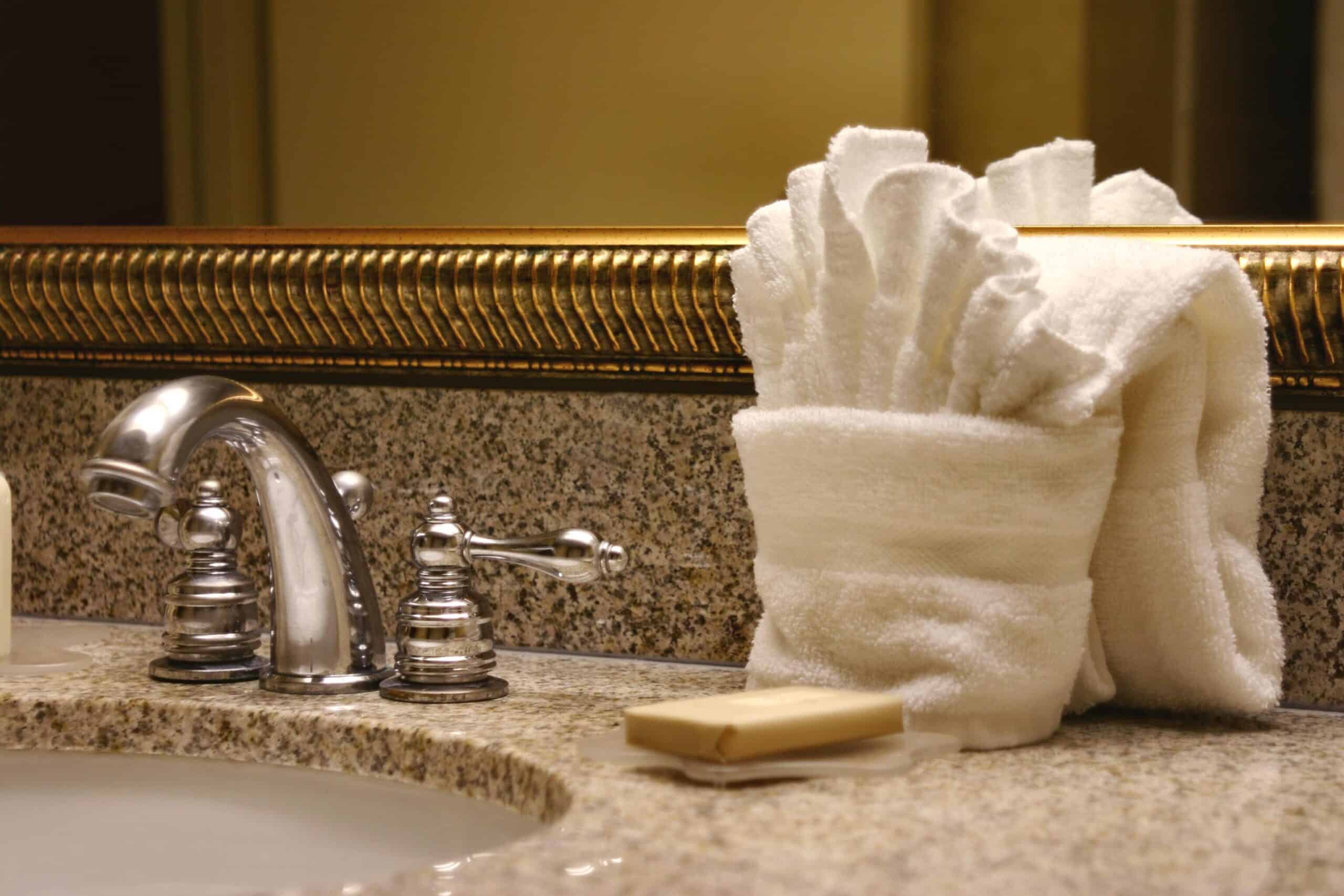 Elegant hotel bathroom counter with chrome faucet, folded white towels, and a bar of soap on granite countertop