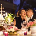 Couple laughing together at an elegantly decorated candlelit event table with crystal glassware and floral centerpieces