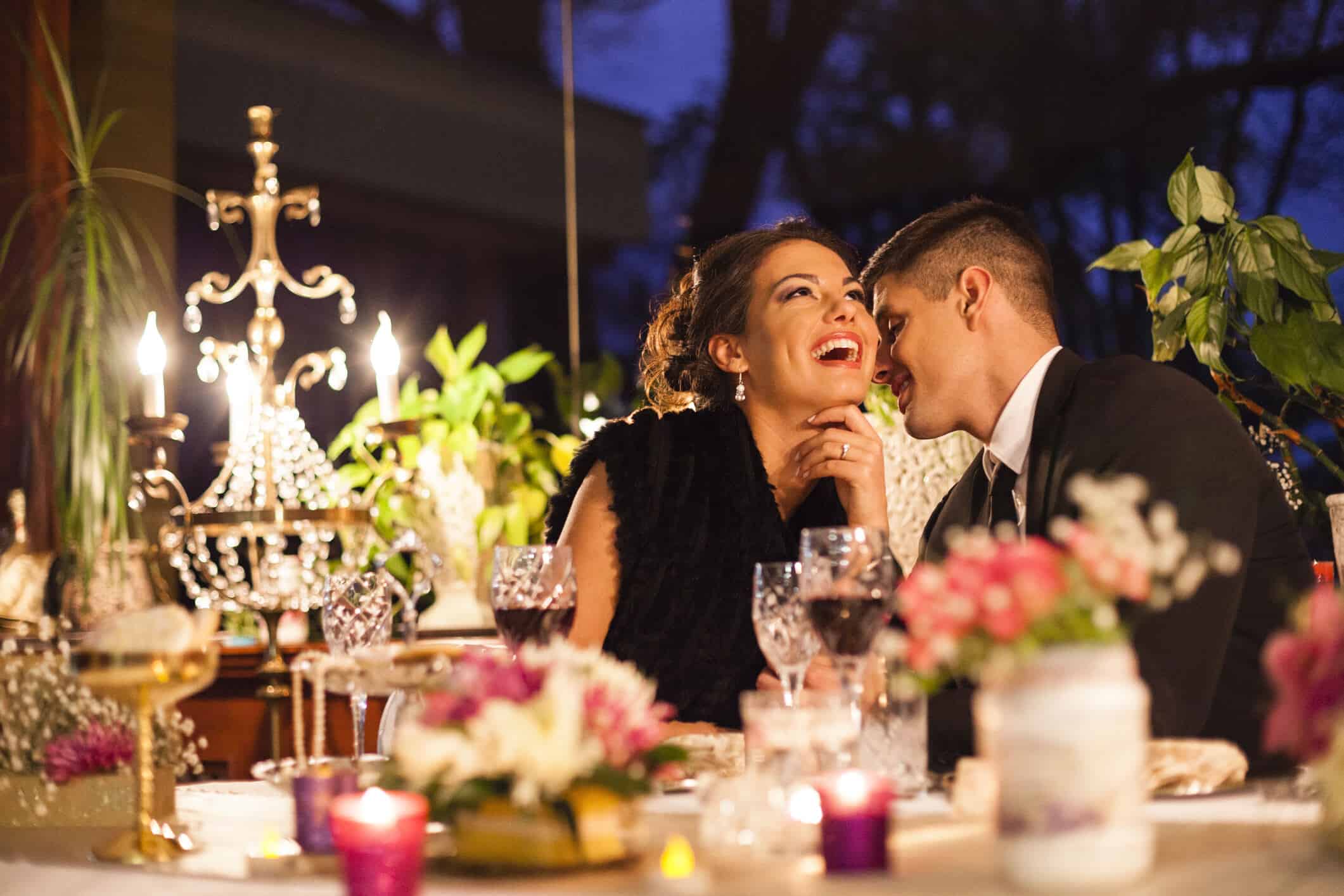 Couple laughing together at an elegantly decorated candlelit event table with crystal glassware and floral centerpieces