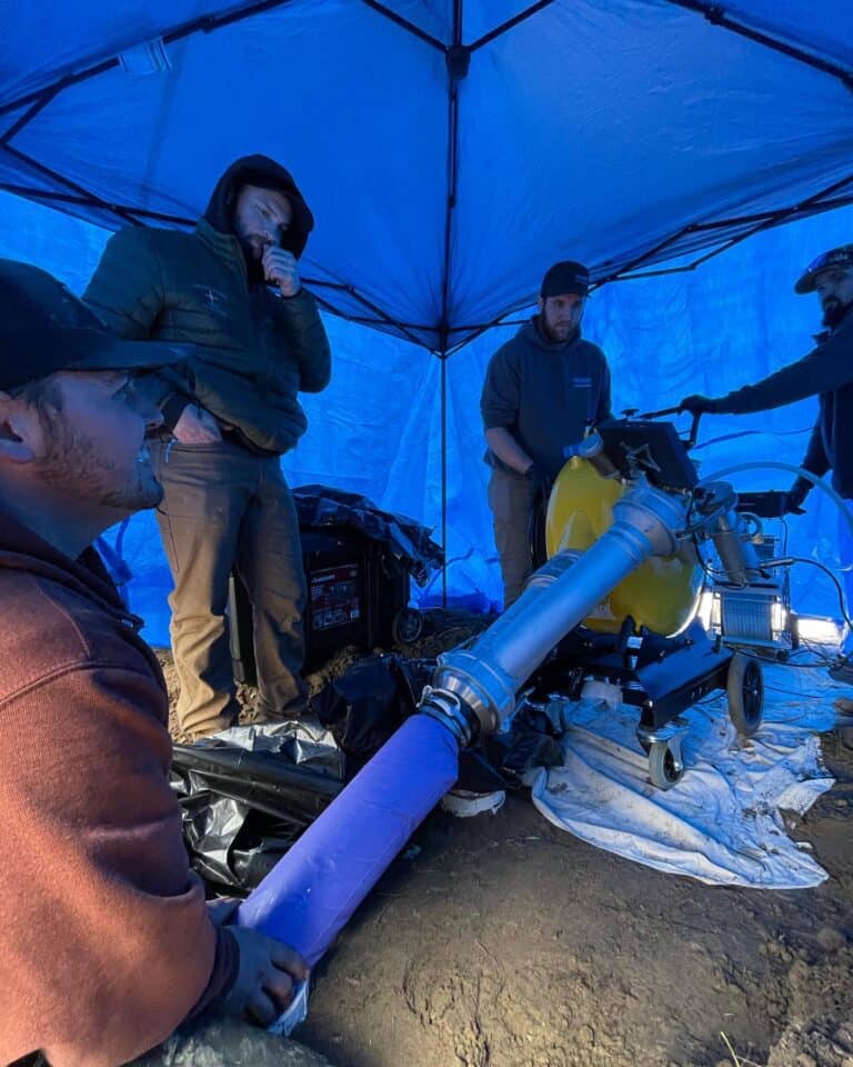 Trenchless pipe repair using hydro jetting technology under a blue tent.