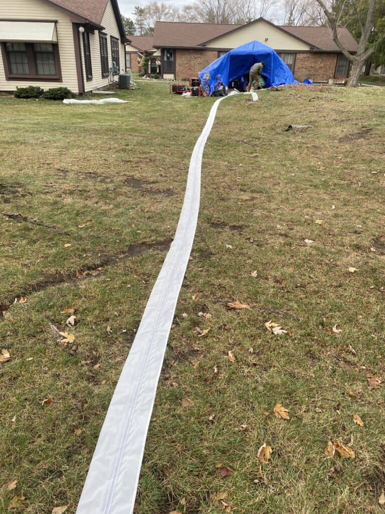 Hydro jetting hose extending across a lawn towards a house, used for drain cleaning services.