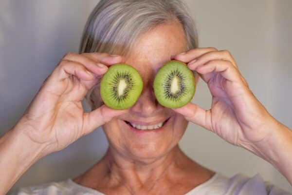 Elderly woman holding a ripe green kiwi cut in half in front of her eyes. Concept of fruit rich in vitamins and healthy eating.