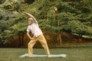 Senior man in white t-shirt standing at park and doing excercises. Positive mature woman has fitness or yoga class in nature. Wellness and healthy lifestyle on retirement.