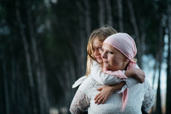 A woman with cancer is next to her daughter. A girl is hugging a woman happy