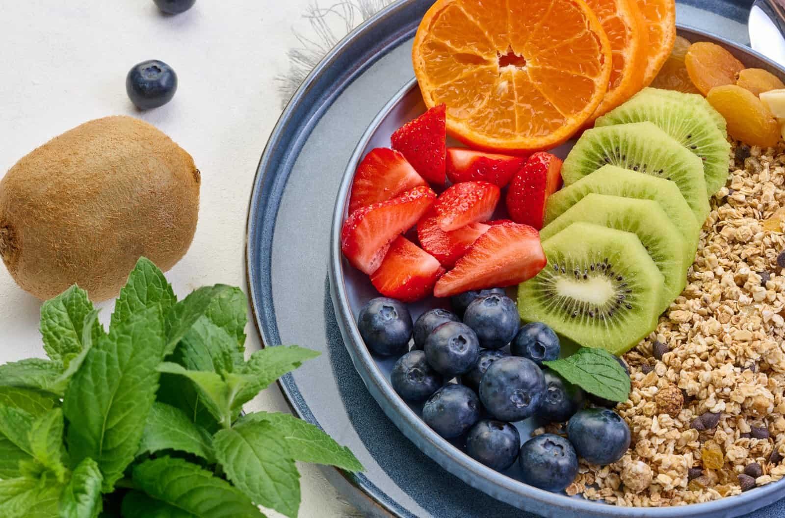 Granola with strawberries, kiwi, banana and blueberries in a round plate on a white table. Healthy and delicious food