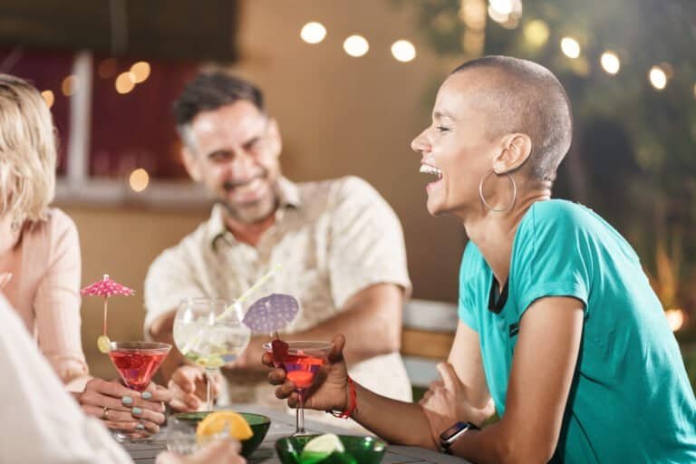 Mature friends drinking cocktails and having great time together - Cheerful woman with shaved hair laughing