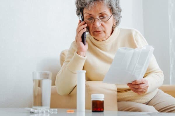 Mature sick woman patient consultation with doctor by phone, prescription for dosage of treatment at home. Senior woman talking on smartphone with doctor, sitting on chair with medicine instruction.