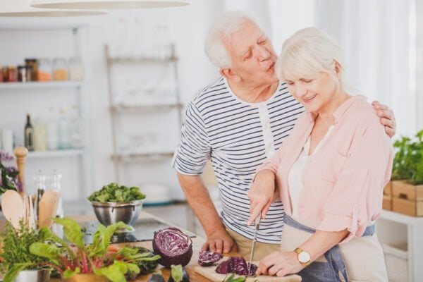 Older Man Is Kissing Wifes Head While She Is Cutting Cabbage On A Vegetarian Dinner