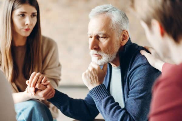 Senior man receiving comfort and support from family during therapy session. Mental health care concept