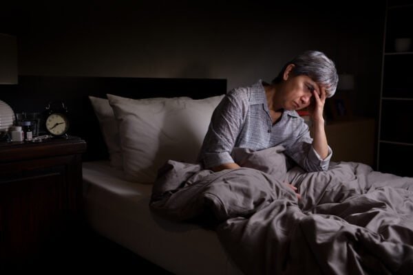 Depressed senior woman sitting in bed cannot sleep from insomnia