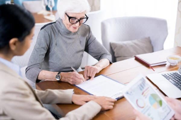 Senior woman wearing eyeglases writing testament with notary agent sitting near by her