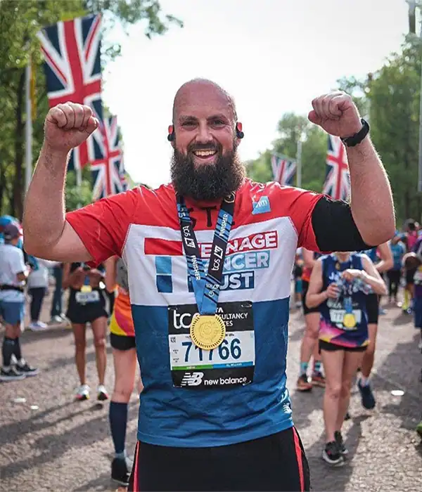 Smiling man celebrates marathon with medal, UK flags nearby.