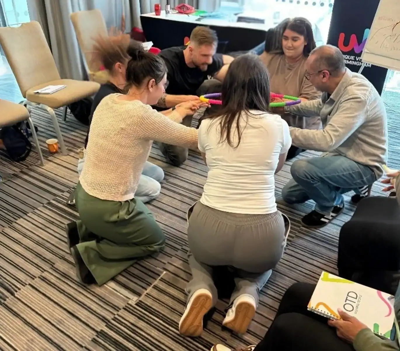 Group teamwork exercise with colorful tubes indoors.