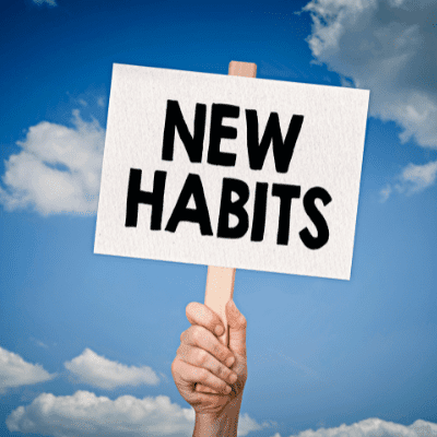 Hand holding a sign saying "New Habits" against a blue sky with clouds.