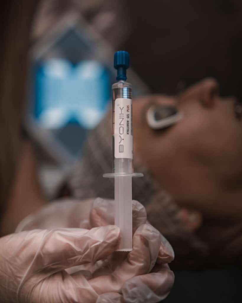 Syringe with skincare serum held near a woman's face during a facial treatment.