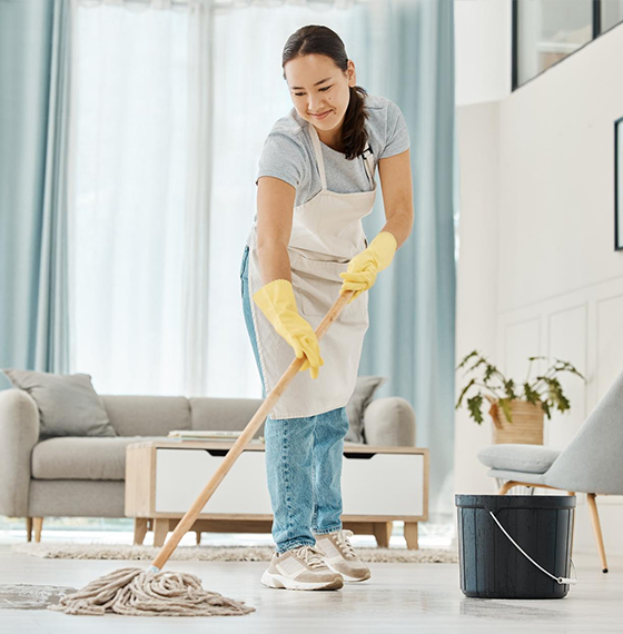 Deep cleaning woman mopping hardwood floor with bucket in living room.