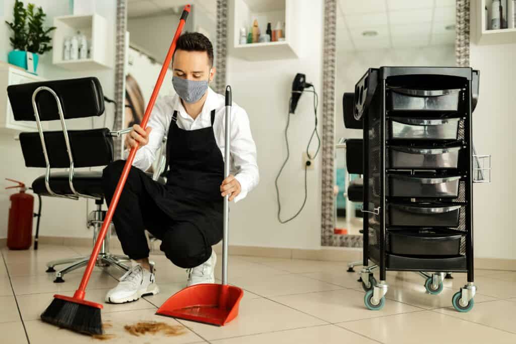 Professional cleaner sweeping up dirt in a salon or barbershop.
