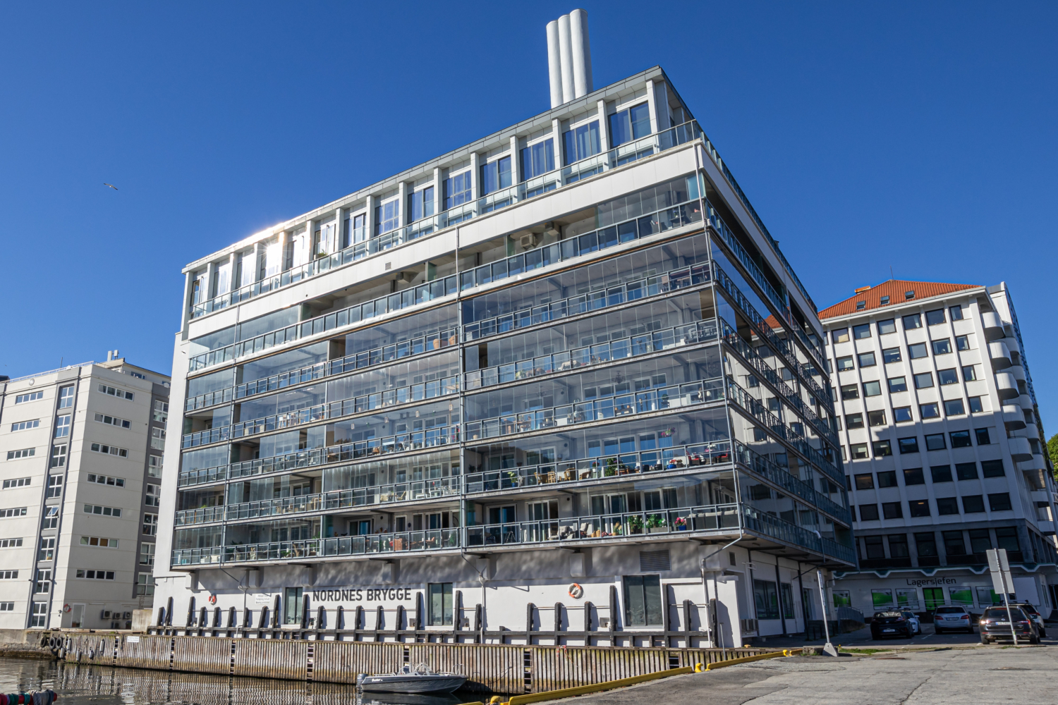 Modern coastal apartment building with waterfront view, glass balconies, and cityscape, Norway.