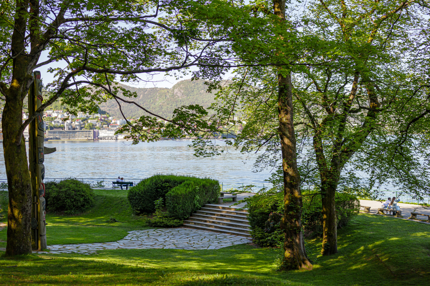 Lush park by the fjord with trees, benches, and scenic mountain views in Norway.