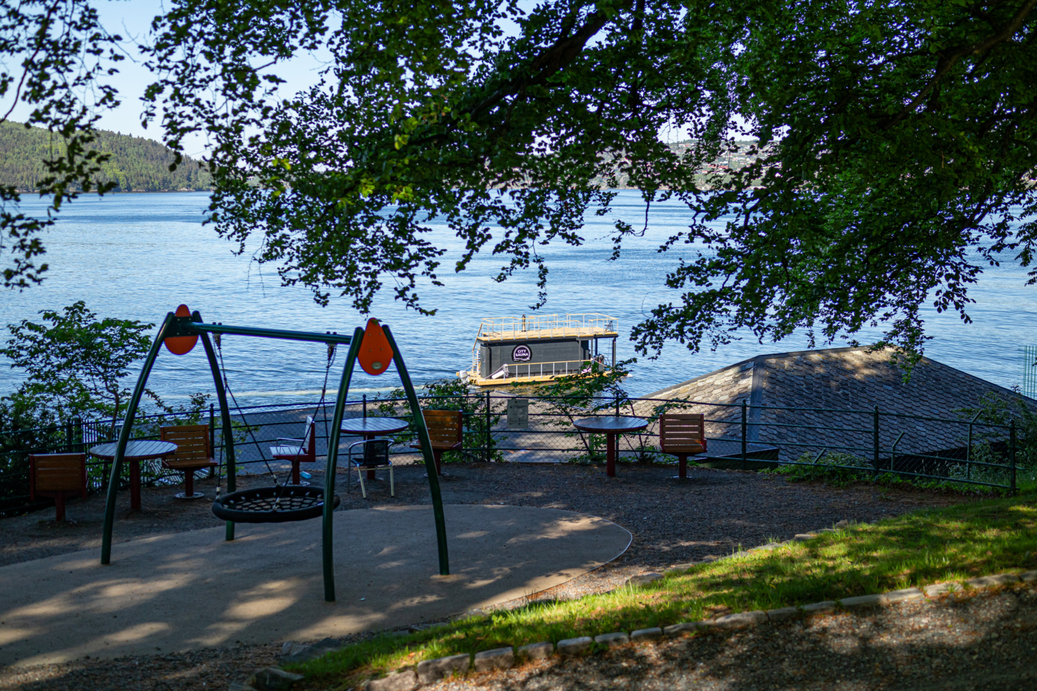 Scenic waterfront park with swings, seating, and view of the fjord and boat. Perfect for relaxing and enjoying Norway's stunning natural beauty.