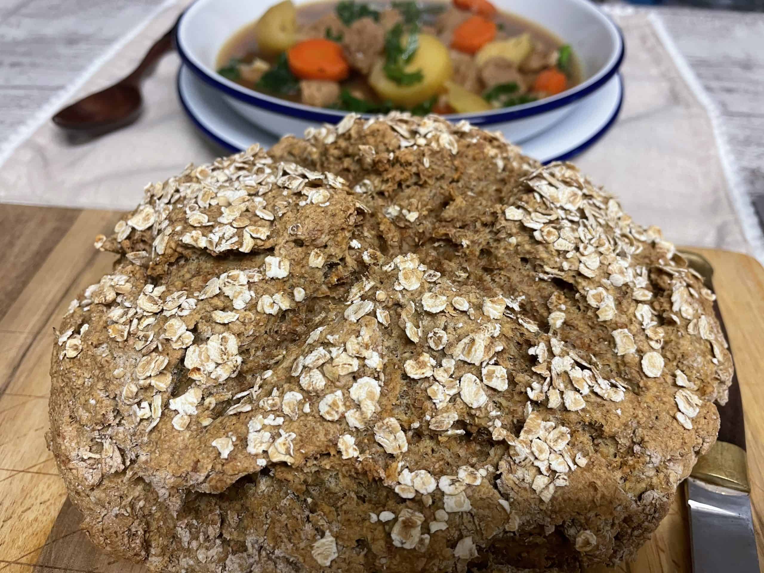 Irish soda bread close up, with bowl of vegan Irish stew in distance.