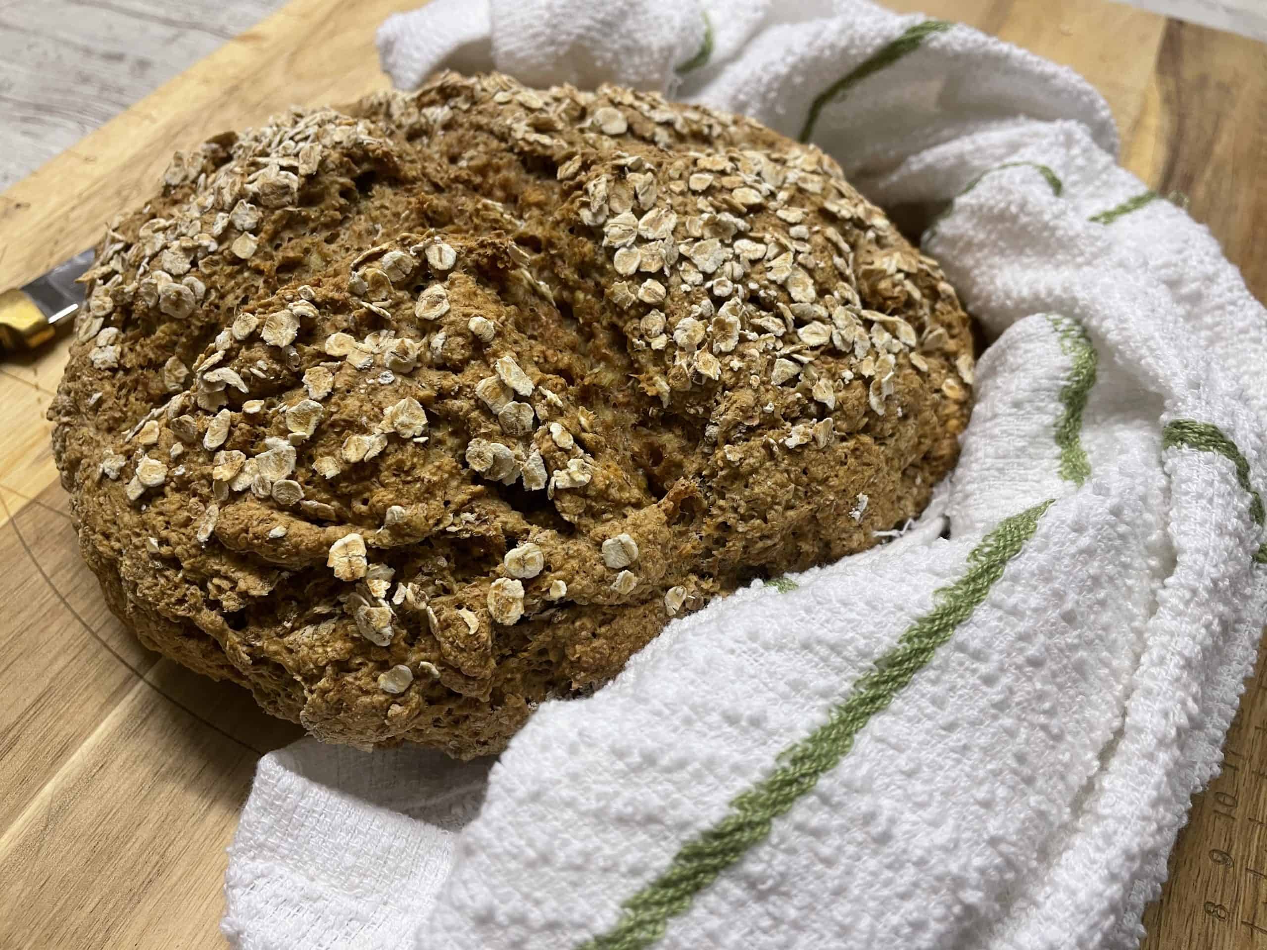 Vegan Irish Soda Bread sitting on wooden chopping board with white tea towel with green stripe.