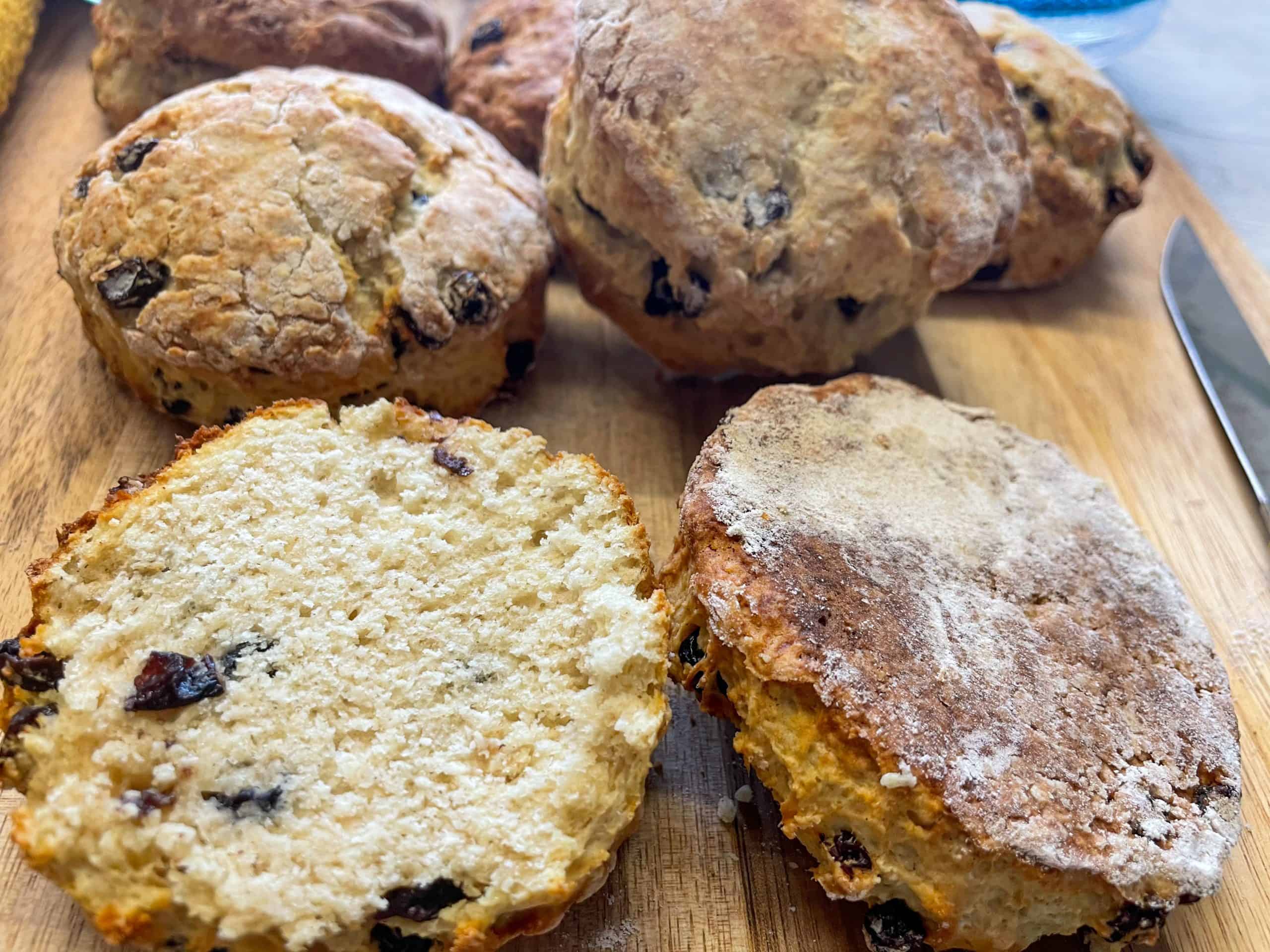 Edinburgh fruit scones, one sliced in half, on wooden chopping board.