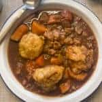 Slow cooker vegan beef stew and dumplings ready to eat in white bowl with blue rim, spoon at side of plate