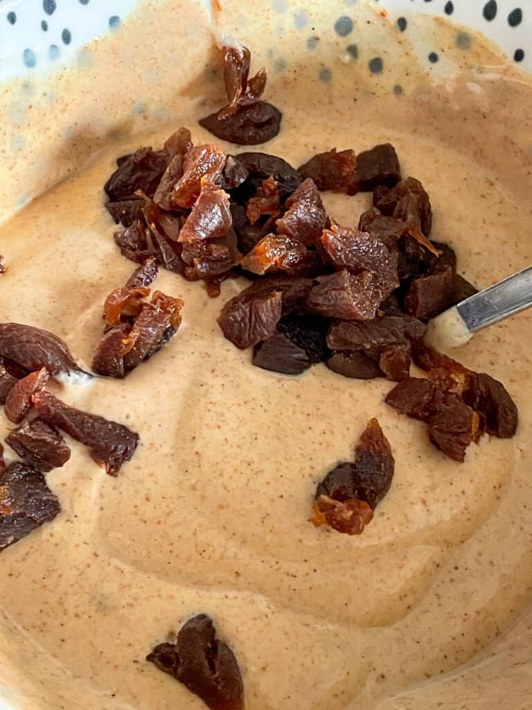 Dried chopped apricots in mixing bowl with spoon and Coronation sauce.