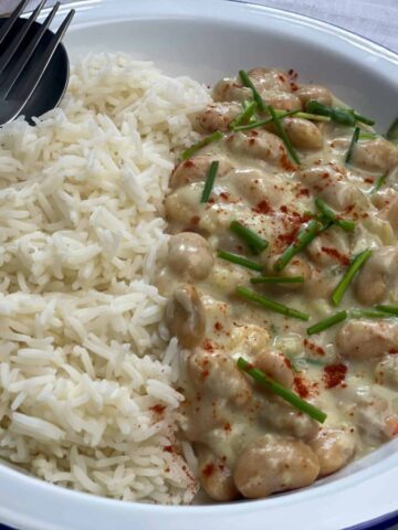 Butterbean chicken supreme with white boiled rice served on a white bowl with a spoon and fork displayed at the side