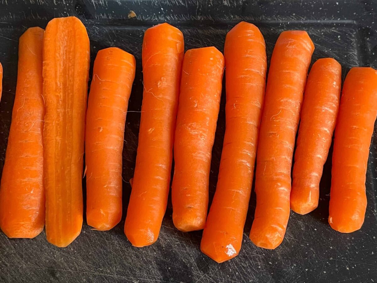 a line of carrots, peeled, topped and tailed on a black chopping board.