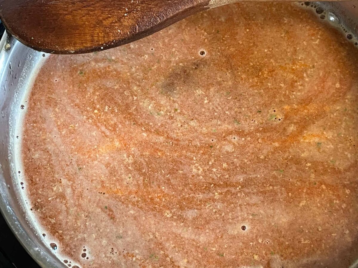 carrot hotdogs underneath the cooking stock and flavourings in the pan with wooden spoon to side.